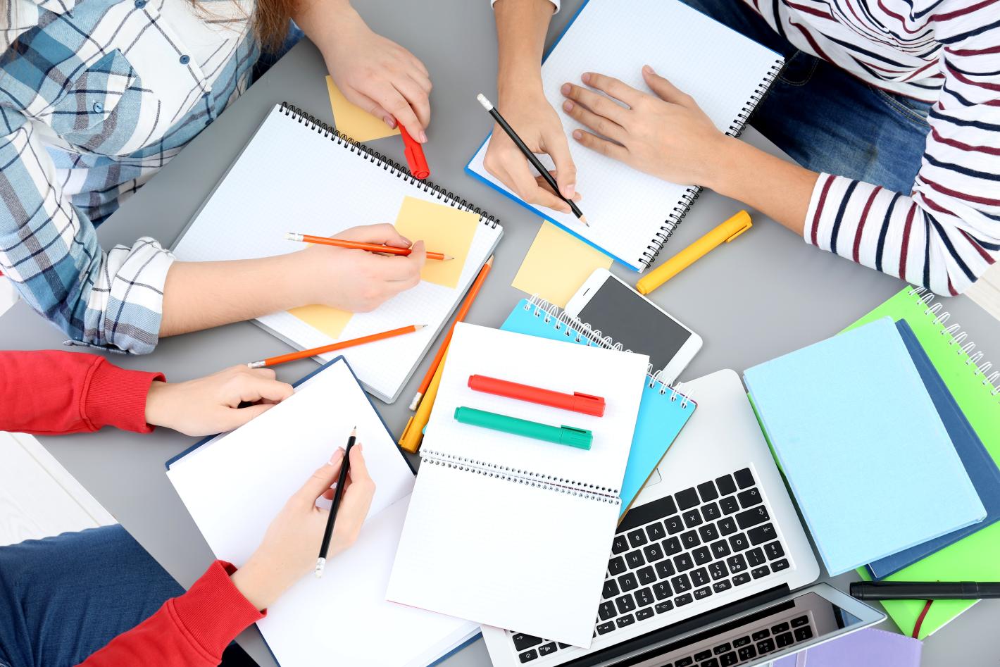 Overhead view of students focused on their assignments, collaborating at a shared desk in a study environment.