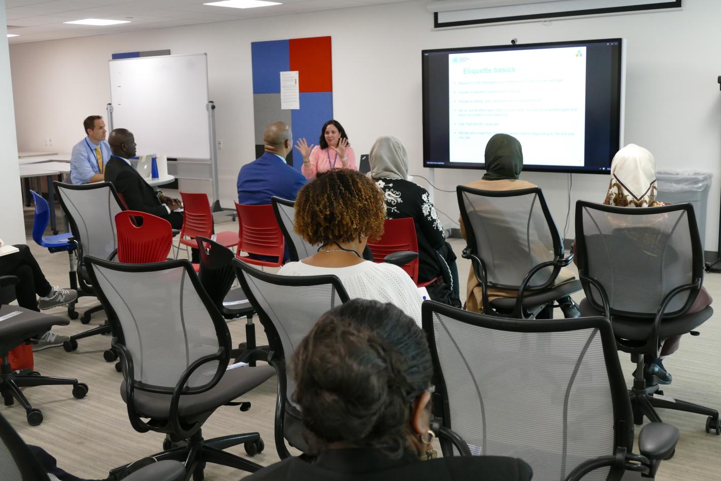 A diverse group of individuals seated in chairs, engaged in conversation at a workshop within a well-lit room.