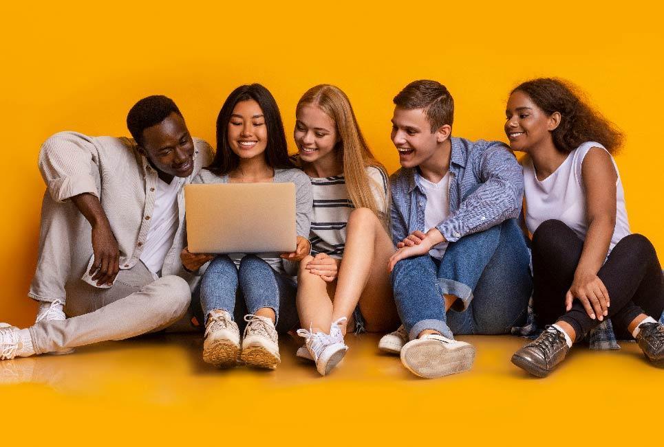 A diverse group of young individuals seated on the floor, engaged with a laptop in a collaborative setting.